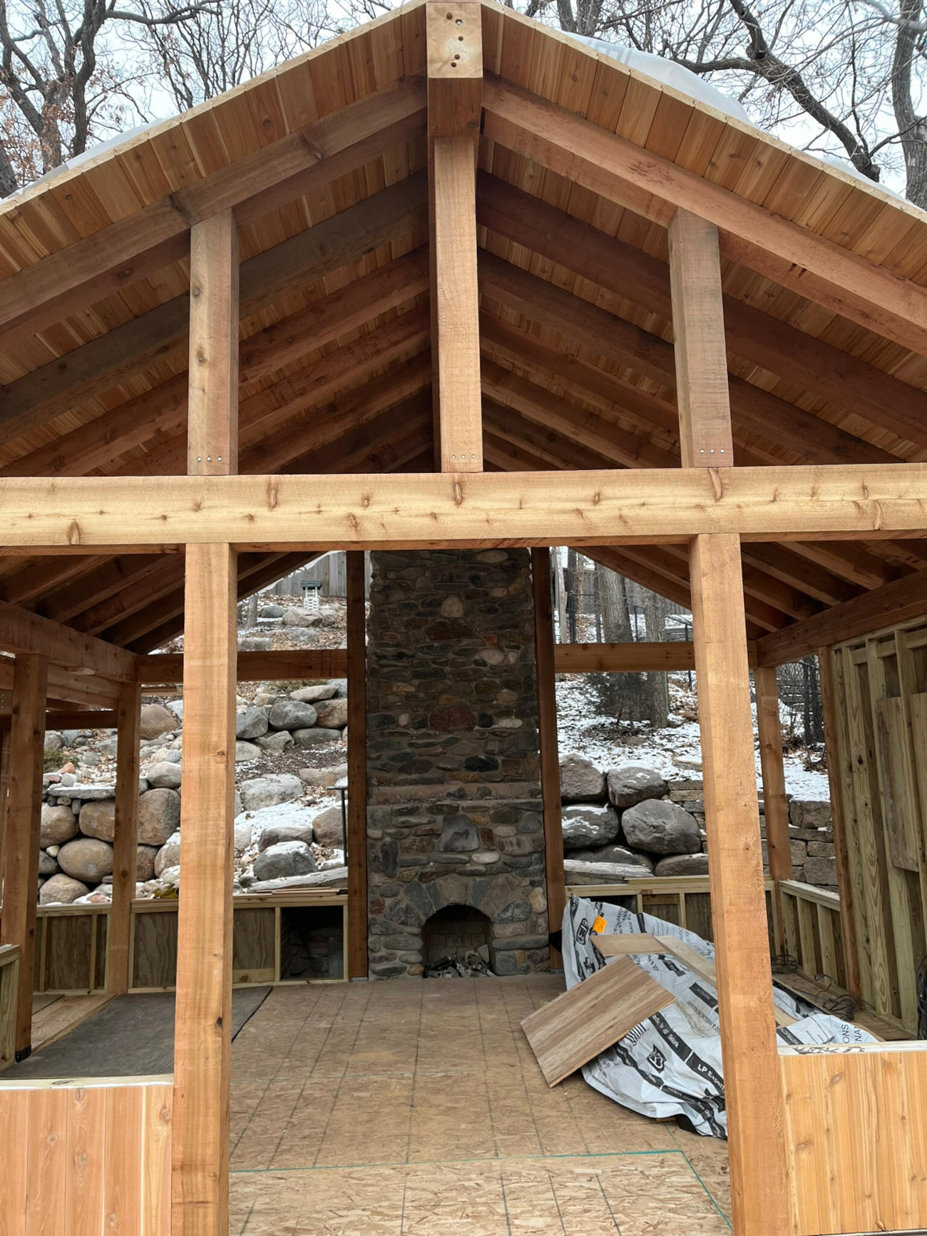 Framed outdoor structure with exposed beams and stone fireplace under construction