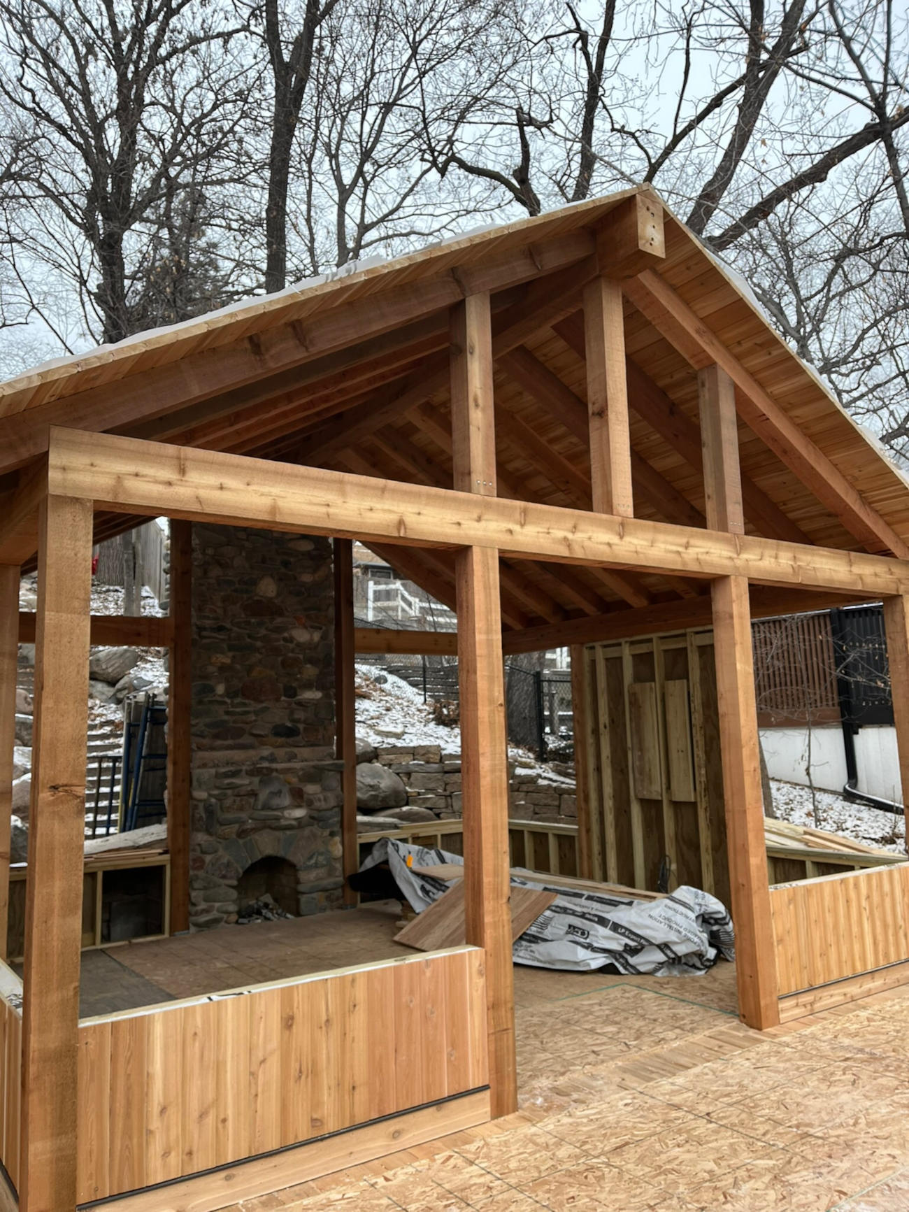Outdoor structure under construction with exposed beams and stone fireplace