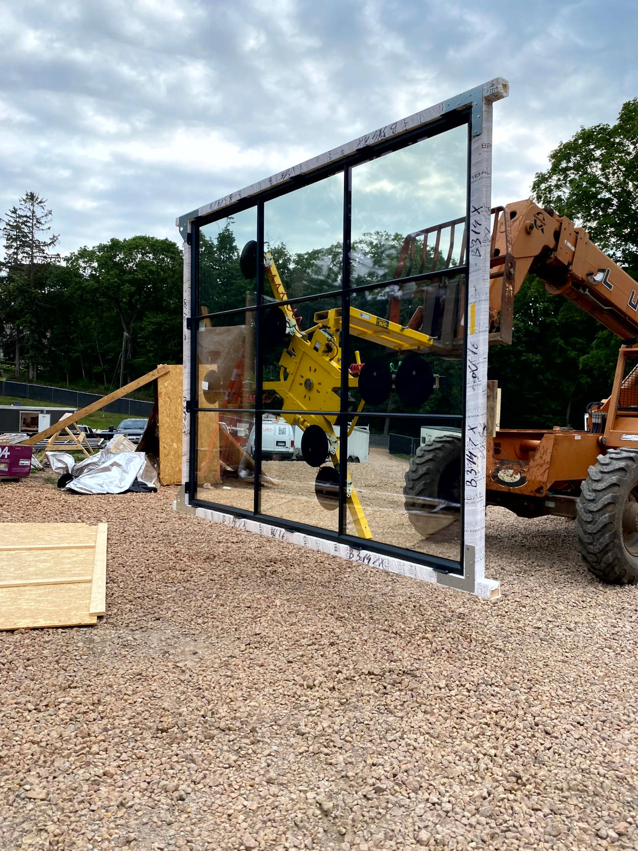 Large glass wall panel being lifted by excavator for home installation